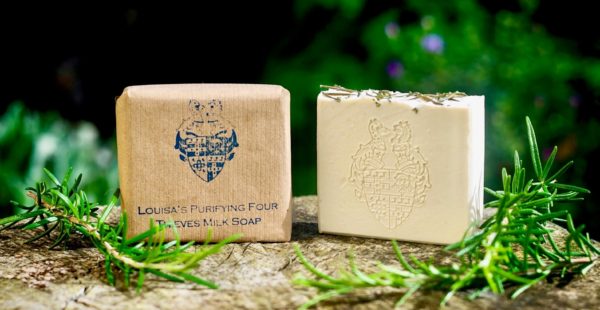 2 Louisa's Purifying Four Thieves Milk Soaps one wrapped in brown paper and one unwrapped on a stone slab with pieces of rosemary either side of the soaps